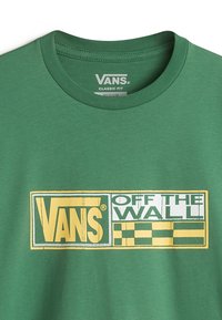 Camiseta de algodón verde con cuello redondo. Presenta un gran logo en amarillo y blanco de "VANS OFF THE WALL" con un patrón de cuadros. Corte clásico.