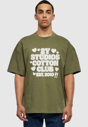 Olivegrünes Baumwoll-T-Shirt mit oversized Passform. Zentrale weiße grafische Schrift liest "2Y STUDIOS COTTON CLUB EST. 2010", umgeben von Herzformen.