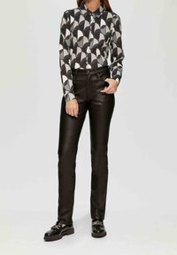 Czarne skórzane spodnie w połączeniu z długim rękawem koszulą z geometrycznym wzorem w odcieniach czerni, bieli i szarości. Koszula ma kołnierzyk i guziki.