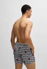 Black boxer shorts featuring a repeated logo pattern in white and red. Comfortable fit with elastic waistband and smooth fabric texture.