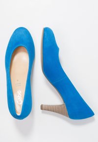 Blue suede high heels with a rounded toe and a textured, stacked heel. Features a smooth inner lining and subtle branding on the insole.