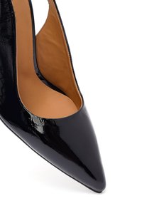 Décolleté in vernice nera con tacco alto e punte affusolate, caratterizzato da un design cut-out, con un interno liscio beige e una silhouette minimalista.
