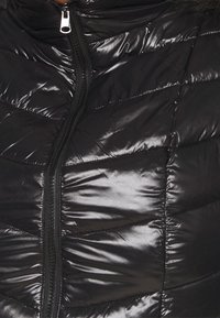 Schwarze Steppjacke mit glänzender Oberfläche, gestepptem Design mit Zickzackmustern und zentralem Reißverschluss.