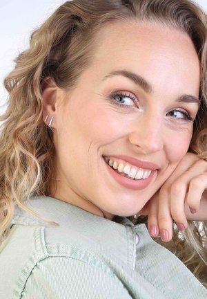 Boucles d'oreilles linéaires en argent présentées sur un modèle aux cheveux ondulés, sur fond clair. Le modèle porte une veste vert clair.