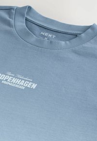 Lys blå t-shirt lavet af bomuld, med en rund halsudskæring og et trykt design, der inkluderer "COPENHAGEN" i fed hvid skrift.