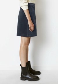 Gonna mini in suede blu navy con taglio dritto, abbinata a stivaletti neri in pelle con pannelli elastici laterali e suole in gomma spessa.