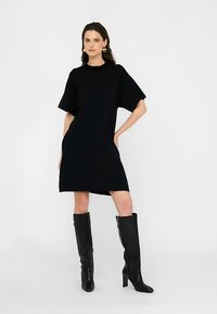 Zwarte gebreide jurk met korte mouwen, losse pasvorm, ronde halslijn en lengte boven de knie, gecombineerd met hoge zwarte laarzen.
