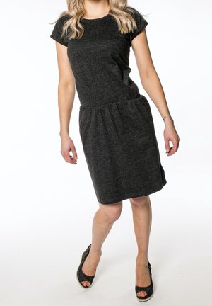 Kvinde iført en knælængde mørkegrå kortærmet kjole med et subtilt mønster og sorte åbne kilehælssko, stående mod en hvid baggrund.