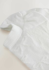 Biela pletená čiapka s textúrovaným vzorom. Má rebrovaný lem a jemne našitú mašľu na boku. Mäkko, ľahký materiál.