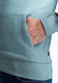 Világoskék kapucnis pulóver, puha pamutból készült, kenguruzsebb, bordás mandzsetta és alsó szegély jellemzi. Egyszerű dizájn, minimális varrási részletekkel.