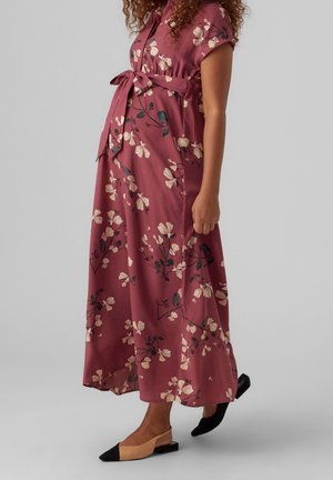Pregnant woman wearing a ankle-length dusty rose floral dress with short sleeves and a tied waist belt, paired with beige and black flat shoes.