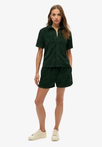 Groene terrycloth tshirt met korte mouwen en een kraag, gecombineerd met bijpassende shorts. Bevat een gestructureerd bladpatroon en zijzakken. Sneakers maken de look compleet.