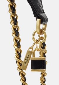 Sangle en chaîne noire composée de maillons en métal doré entrelacés et de maillons en plastique brillant, rehaussée d'un cadenas doré et d'une étiquette de marque avec une gravure "GUESS".