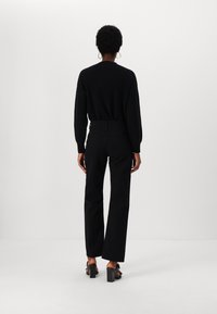 Maglione nero a maglia, pantaloni neri a vita alta e sandali con tacco spesso. Texture liscia e design semplice, visto da dietro.