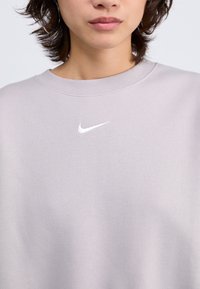 Ljusgrå sweatshirt i mjukt material med rund halsringning och ribbade ärmslut, med en liten vit Nike-logotyp på bröstet.