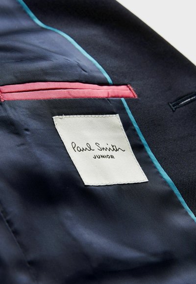 Marinblått tyg med en slät yta har kontrasterande akvamarin- och rosa detaljer. En vit etikett visar "Paul Smith JUNIOR" i svart handstil.