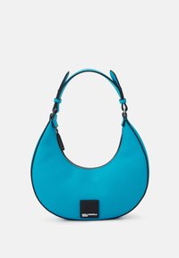 Turkos axelväska med en böjd, unik form. Har svarta detaljer och dragkedjestängning. Slät textur och robust handtag.