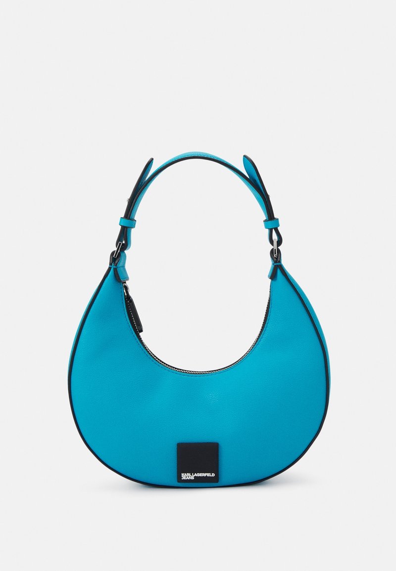 Turkos axelväska med en böjd, unik form. Har svarta detaljer och dragkedjestängning. Slät textur och robust handtag.