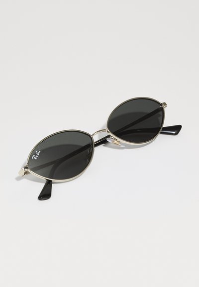 Слънчеви очила Ray-Ban с черни овални лещи, тънка златна метална рамка и черни пластмасови крачета. Включват подложки за носа за комфорт.