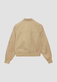 Veste bomber beige avec un col rond, des poignets côtelés, une taille élastique et une poche à patch sur la manche gauche. Texture de tissu lisse.
