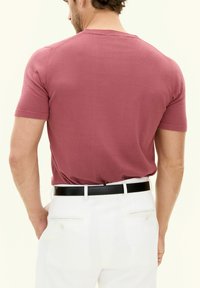 T-shirt a maniche corte, aderente, di colore rosa tenue, realizzata in un tessuto morbido, abbinata a pantaloni bianchi su misura e una cintura nera slim.