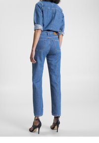 Ljusblå denimjeans med hög midja och rak passform. Har bakfickor och en brun läderlapp vid midjan.