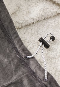 Tissu en polaire gris avec une doublure blanche texturée. Présente un cordon de serrage avec un fermoir noir et des coutures noires le long du bord.
