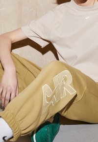 Beige cotton t-shirt with Nike logo, paired with yellow sweatpants featuring large "AIR" text, and green sneakers with textured soles.