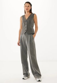 Grå, skräddarsydd väst med V-ringning, fem knappar och en åtsittande form, i kombination med lösa, veckade grå byxor. Bärs med vita sneakers.