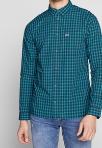 Camicia con bottoni caratterizzata da un motivo a quadri turchese e blu navy, maniche lunghe e una tasca sul petto con un piccolo logo. Tessuto di cotone.