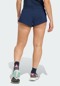 Granatowe szorty sportowe z perforowaną fakturą, z zaokrąglonym dołem. W połączeniu z szarymi i turkusowymi butami do biegania oraz granatowymi skarpetkami z różowymi akcentami.