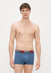 Vīriešu zilas bokseršorti no kokvilnas maisījuma ar melnu jostas joslu, kurā ir sarkans un balts „DIESEL” uzraksts, un pieguļoša forma.