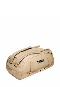 Sac de voyage beige avec deux poignées et des bretelles. Tissu résistant, compartiments zippés et logo de la marque sur un côté.