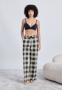 Sutiã preto combinado com calças de pijama largas em padrão xadrez nas cores preto, branco e bege. As calças apresentam uma cintura elástica com cordão e bolsos.