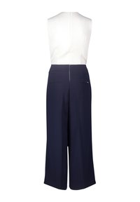 Ujjatlan overál fehér felsőrésszel és tengerészkék, bő szárú nadrággal. Hátul cipzárral és két hátsó zsebbel rendelkezik. Simaság jellemzi az anyagát és letisztult vonalait.