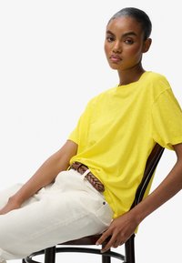 Gul bomulds T-shirt med løs pasform, korte ærmer og rund hals, parret med cremefarvede bukser og et vævet brunt bælte.