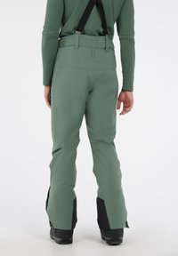 Groene waterdichte skibroek met verstelbare zwarte bretels, wijde pijpen en zwarte accenten bij de enkels. Soepele textuur en op maat gesneden pasvorm.