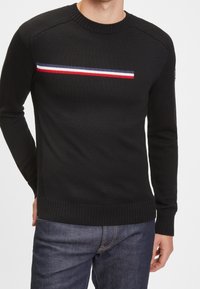 Schwarzer Strickpullover mit langen Ärmeln, der ein horizontal gestreiftes Muster in Rot, Weiß und Blau über der Brust aufweist. Gerippter Rundhalsausschnitt.