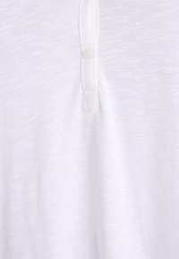 Balta trumpomis rankovėmis marškinėliai iš minkštos, tekstūruotos medžiagos, su apykakle ir vienu mygtuko užsegimu prie kaklo.