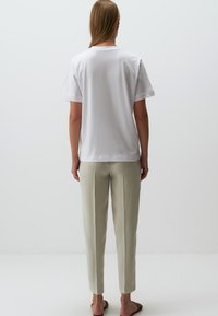 Weißes Baumwoll-T-Shirt mit kurzen Ärmeln, kombiniert mit hellolivgrünen elastischen Hosen, von hinten gesehen, getragen mit braunen Sandalen.