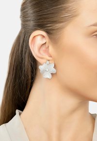 Silver floral earrings with sparkling details and a central pearl, featuring a curved design that adds dimension to the accessory.