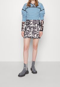 Lichtblauwe cropped sweatshirt met zwarte accenten, gecombineerd met een aansluitende gemusterde minirok in zwart en wit, en grijze enkellaarsjes.