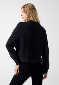 Czarna krótka bluza z okrągłym dekoltem i długimi rękawami, z prążkowanymi mankietami i dołem. Miękka w dotyku, minimalistyczny design.