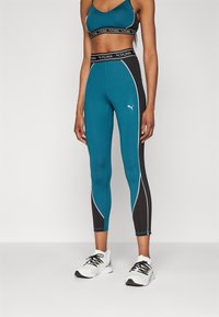Leggings teal e neri con piping bianco a contrasto, dotati di vita alta e logo PUMA, abbinati a un reggiseno sportivo corto coordinato.