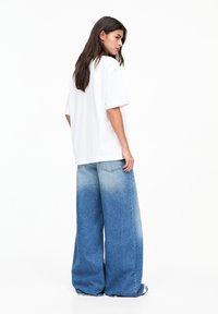 T-shirt oversize blanc associé à un jean à jambes larges présentant un effet ombragé allant du bleu clair au bleu foncé et des poches arrière classiques.