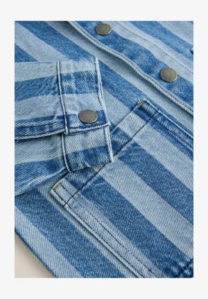 Blå denimjakke med horisontale striber, udstyret med metal snapknapper og kontrasterende syninger. Nærbillede af ærme og brystlomme.