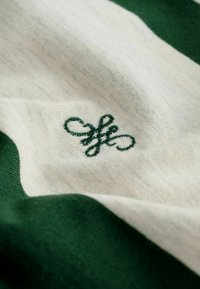Tissu rayé vert et crème avec un délicat logo vert brodé, présentant une texture lisse et un contraste de couleurs subtil.