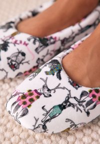 Valged fliisist sussid, millel on värvikirevaid põhjapõdrakujutisi erinevates kostüümides, ümarate varvaste ja hingavate lõigatud külgedega.