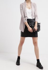 Lichtroze cardigan met een open voorkant, zwarte leren minirok, witte top, zwarte schoenen en een zwarte tas. Eenvoudig ontwerp, gestructureerde materialen.