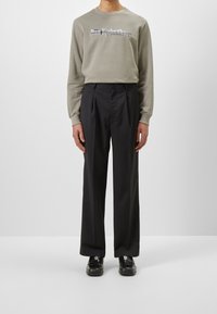 Šedá mikina s výšivkou na přední straně a černými kalhotami na míru. Hladká tkanina, pohodlný střih a černé šněrovací boty.